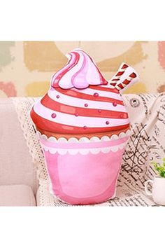 a pink cupcake shaped pillow sitting on top of a white couch next to a coffee mug