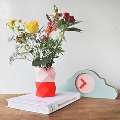 a vase filled with flowers sitting on top of a wooden table next to a clock