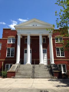 an old brick building with columns and steps leading up to the front door on a sunny day