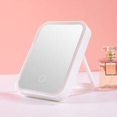 the mirror is next to a bottle of perfume on a pink surface with a pink wall in the background