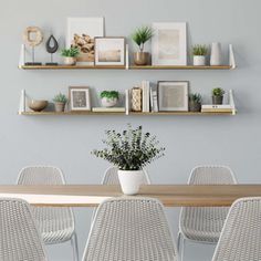 a dining room table with white chairs and shelves on the wall above it that are filled with potted plants