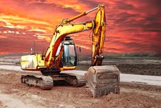 an excavator is parked on the side of a dirt road at sunset