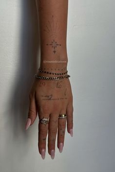 a woman's arm with tattoos and bracelets on her left hand, against a white wall