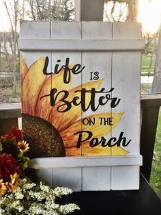 a wooden sign that says life is better on the porch with sunflowers next to it