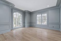 an empty living room with wood floors and gray walls, two windows on the far wall