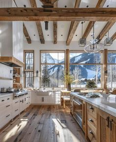 a large kitchen with wooden floors and white cabinets in front of windows that look out onto the mountains