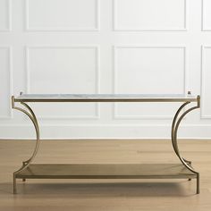 a glass and metal coffee table in front of a white wall with wood flooring