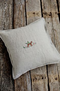 an embroidered pillow sitting on top of a wooden floor next to a piece of wood