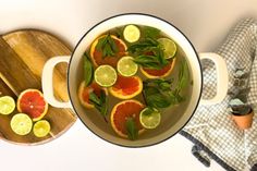 a pot filled with oranges and lime slices on top of a wooden cutting board