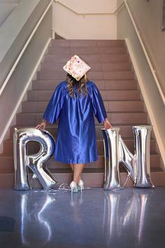 a woman in blue graduation gown standing at the bottom of stairs with letters that spell r and m