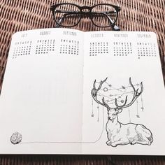 an open notebook with a drawing of a deer and glasses on the table next to it