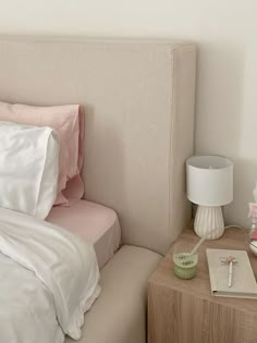 a bed with white sheets and pink pillows on top of it next to a night stand