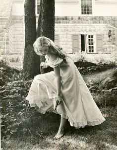 an old black and white photo of a woman leaning on a tree in front of a house