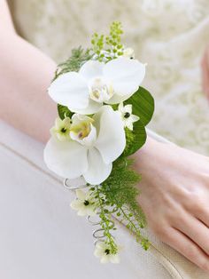 a bride's bouquet with white orchids and greenery sits on her arm