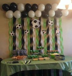 a green table topped with lots of food and desserts next to a wall covered in balloons