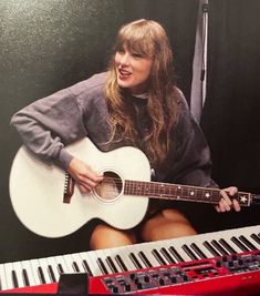 a woman sitting in front of a keyboard and holding a guitar