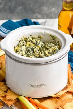 a white crock pot filled with spinach dip surrounded by tortilla chips