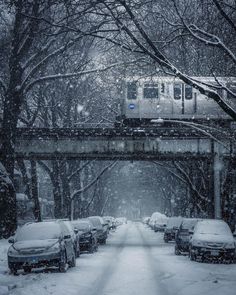 a train is going over a bridge in the snow with cars parked on both sides