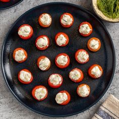 an overhead view of mini tomatoes with cream cheese on them, sitting on a black plate