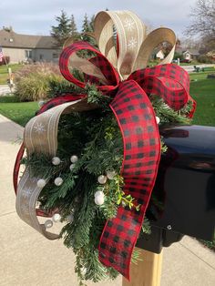 a christmas wreath on top of a mailbox with red and white ribbon tied around it