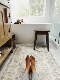 a person's feet resting on a rug in front of a bathtub