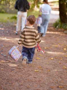 a little boy walking down a dirt road carrying a bag