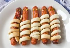 four hot dogs wrapped in banana strips on a white plate with eyes drawn on them