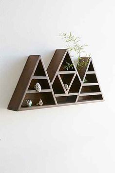 a wooden shelf with three triangular shaped shelves on the wall and a plant growing out of it