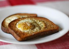 two pieces of toast with an egg in the middle on a white plate sitting on a red and white checkered tablecloth