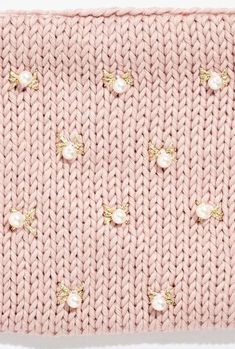 a pink knitted sweater with gold buttons and pearls on the front, in light pink