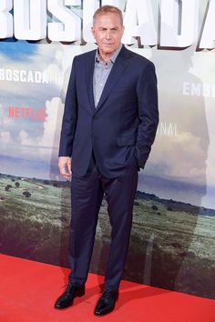 a man in a suit and tie standing on a red carpet at the movie premiere