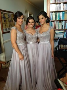 three women in long dresses standing next to each other with bookshelves behind them