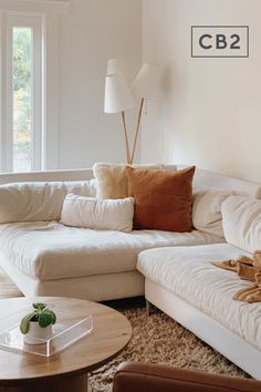 a living room with white couches and pillows on top of the floor, next to a coffee table