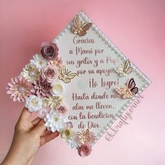 a hand holding a decorated graduation cap with flowers on it and butterflies flying over the top