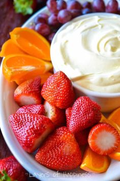 a plate filled with fruit and dip surrounded by grapes, oranges, strawberries