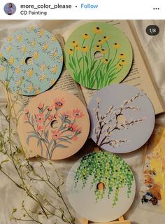 four different designs on paper with flowers and plants painted on them, sitting next to an open book