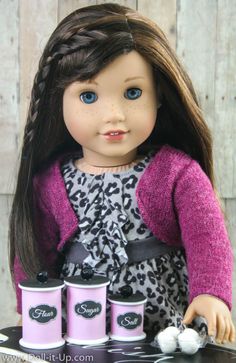 a doll with long hair sitting on top of a table next to three pink containers