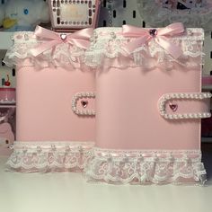 two pink boxes with white lace and bows on them are sitting on a table next to a basket