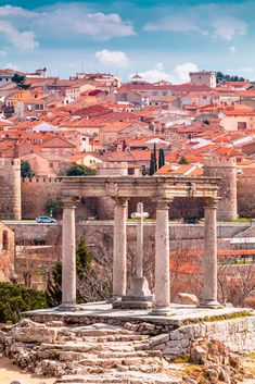 an old roman temple in the middle of a city with red rooftops and tall buildings