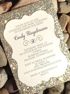 a white and silver wedding card with glitter on the bottom is laying next to some rocks