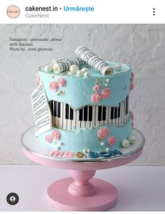 a blue cake decorated with music notes and piano keys on a pink stand in front of a white wall