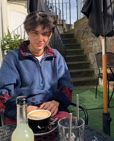 a man sitting at an outdoor table with a cup of coffee in front of him