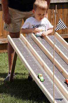 a young boy playing with toy cars on a race track in the grass next to an adult