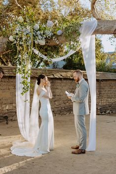 a bride and groom are standing under an arch with white draping on it