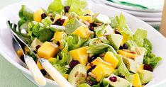 a salad in a white bowl with fruit and cheese on top, along with two forks