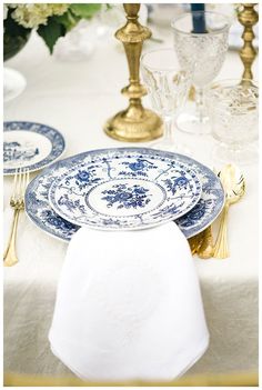 the table is set with blue and white plates, silverware, and gold candlesticks