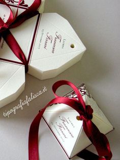 three white boxes with red ribbon tied around the top and one has a tag on it