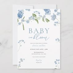 a baby shower card with blue flowers and greenery on the bottom, in front of a white background