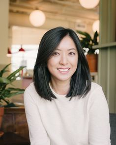 a woman with black hair sitting in front of a potted plant and smiling at the camera