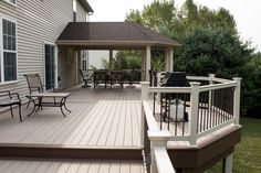 a deck with chairs and grill on the side of it in front of a house